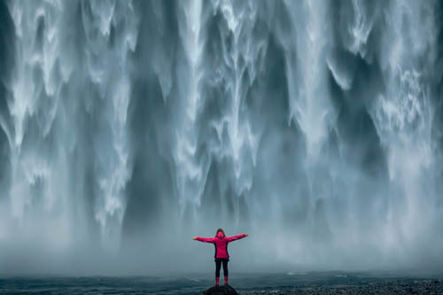 person with outstretched arms under a waterfall