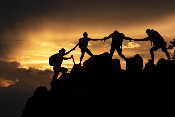 Silhouette of hikers reaching out to help each other
