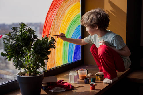 Child painting a rainbow on a window
