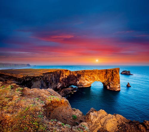 sunset over an ocean with rock formations in the foreground